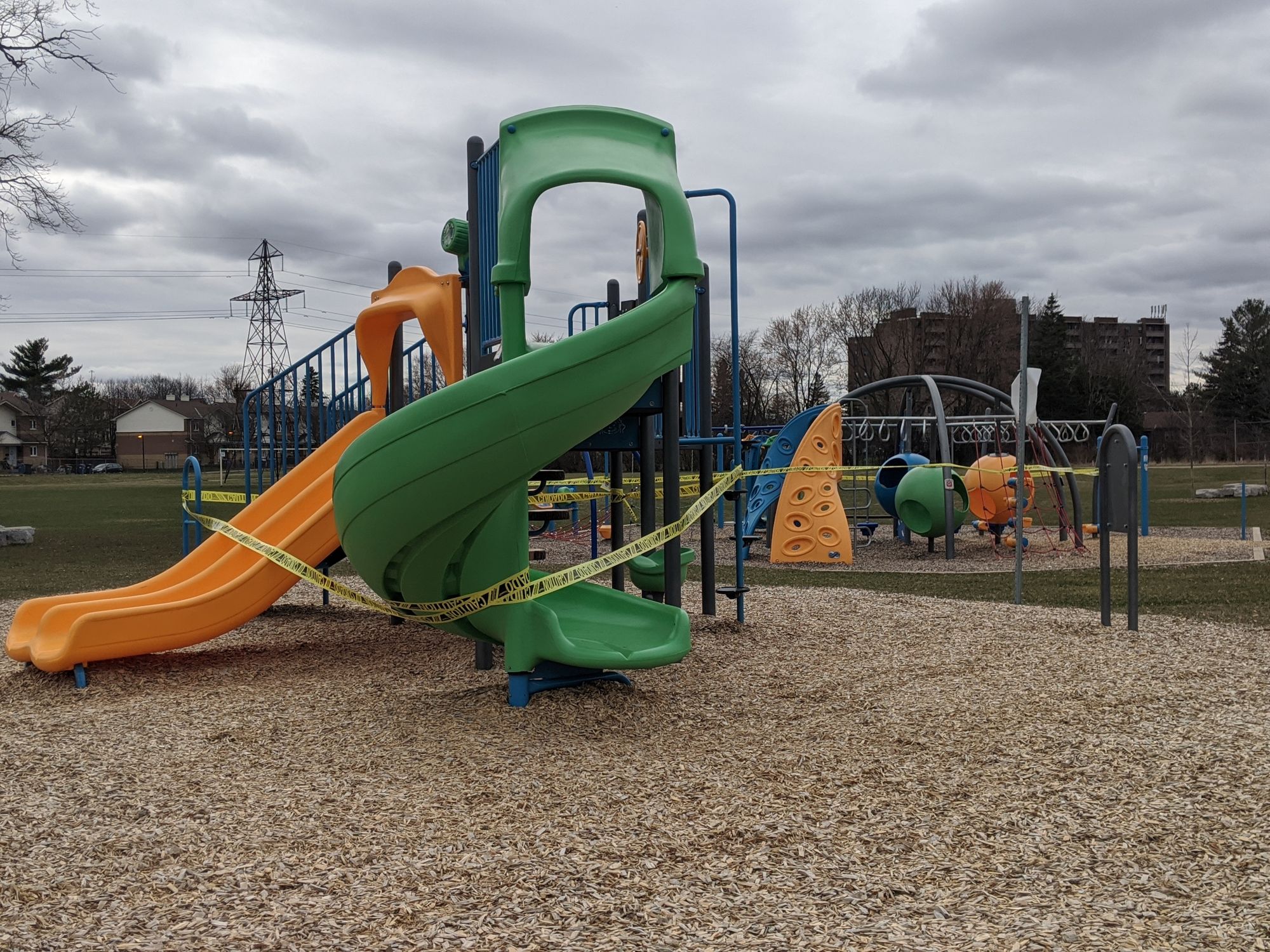 A multi-colored jungle gym in a school yard, the fixtures wrapped in caution tape so people won't use them.