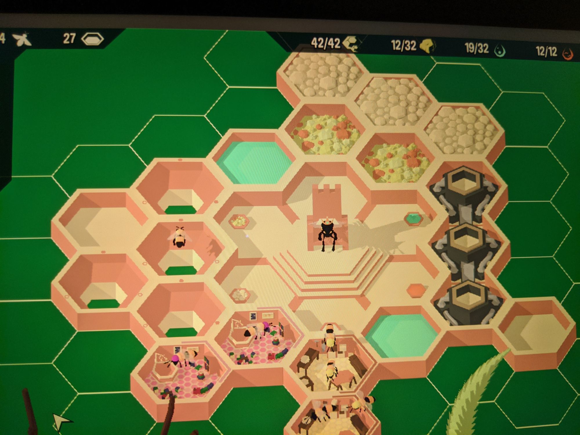 A phone picture of the game Hive Time, a queen bee sits on her thrown and there are hexagon rooms around her with various uses.