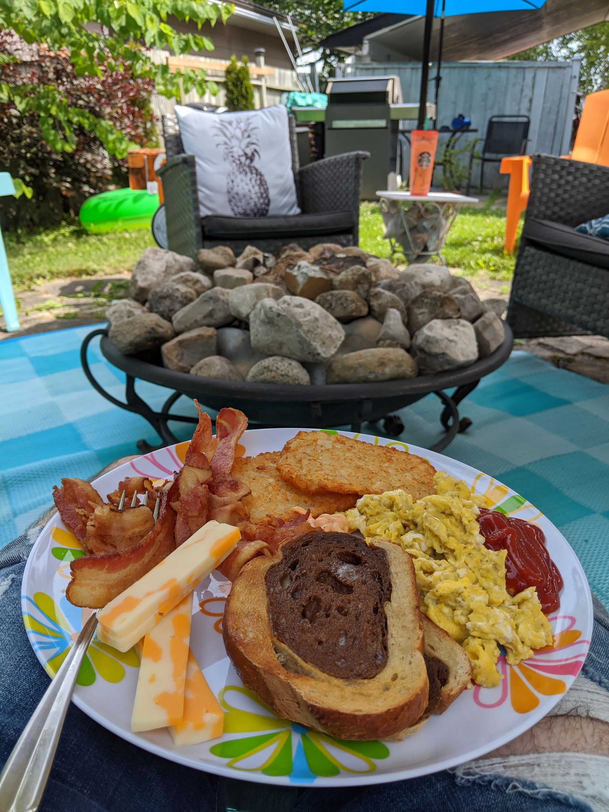 A plate of breakfast food sitting on my lap. In the background behind it a firepit filled with rocks and some patio furniture.