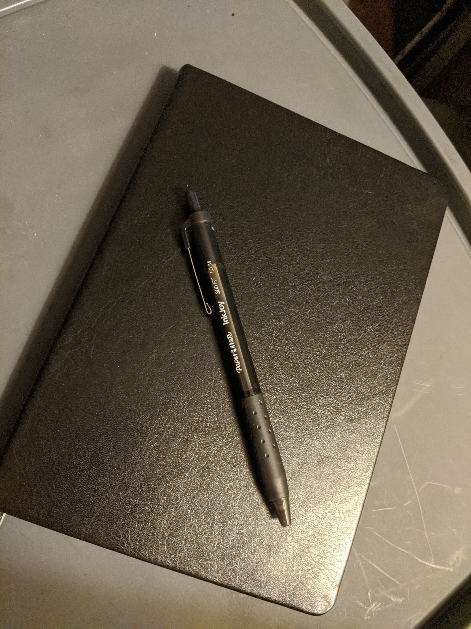 A black journal sitting on a desk, with a black pen resting on top of it.