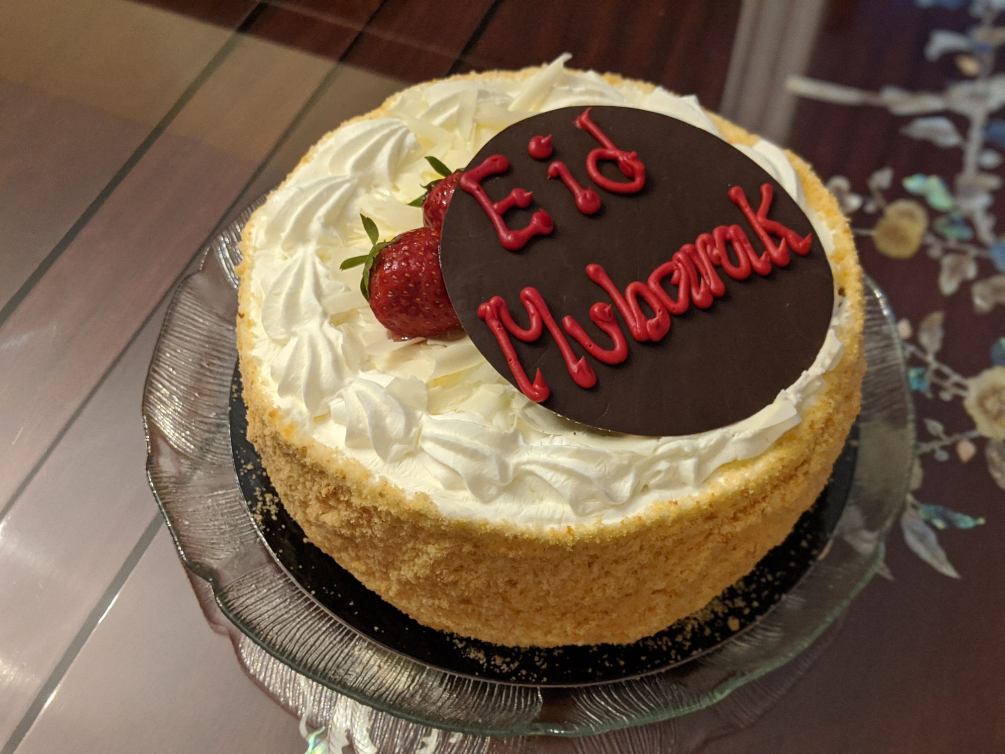 A strawberry shortcake with breadcrumbs around the sides, white icing on top and two strawberries holding up a small chocolate plate that says Eid Mubarak.up 