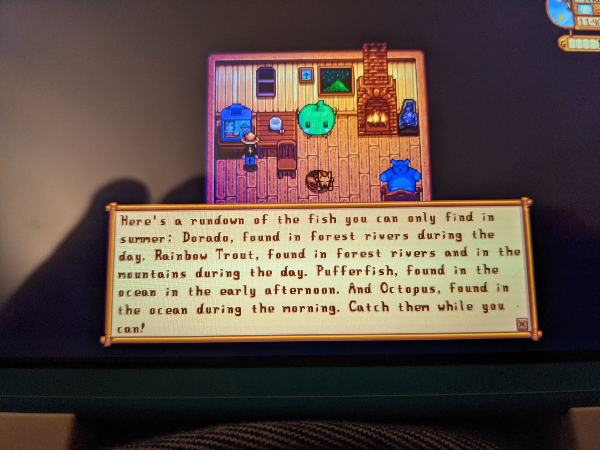 A phone picture of my switch screen, which has my farmer in Stardew Valley looking at the TV which is talking about various fish you can find this current season.