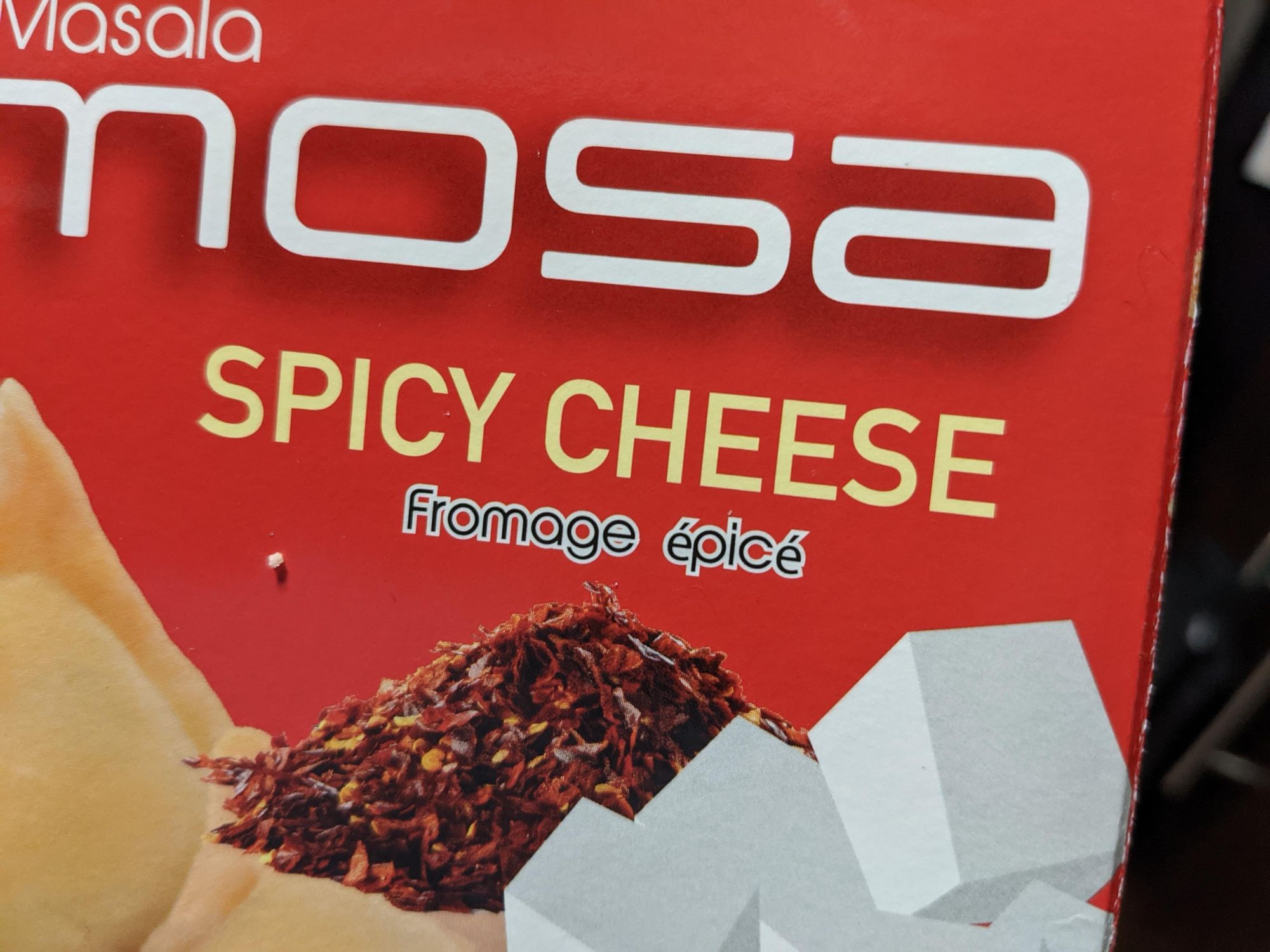 A picture of a box of samosas, they are spicy cheese flavored, with a picture of a pile of spices and what I assume is Feta? cheese cubes.